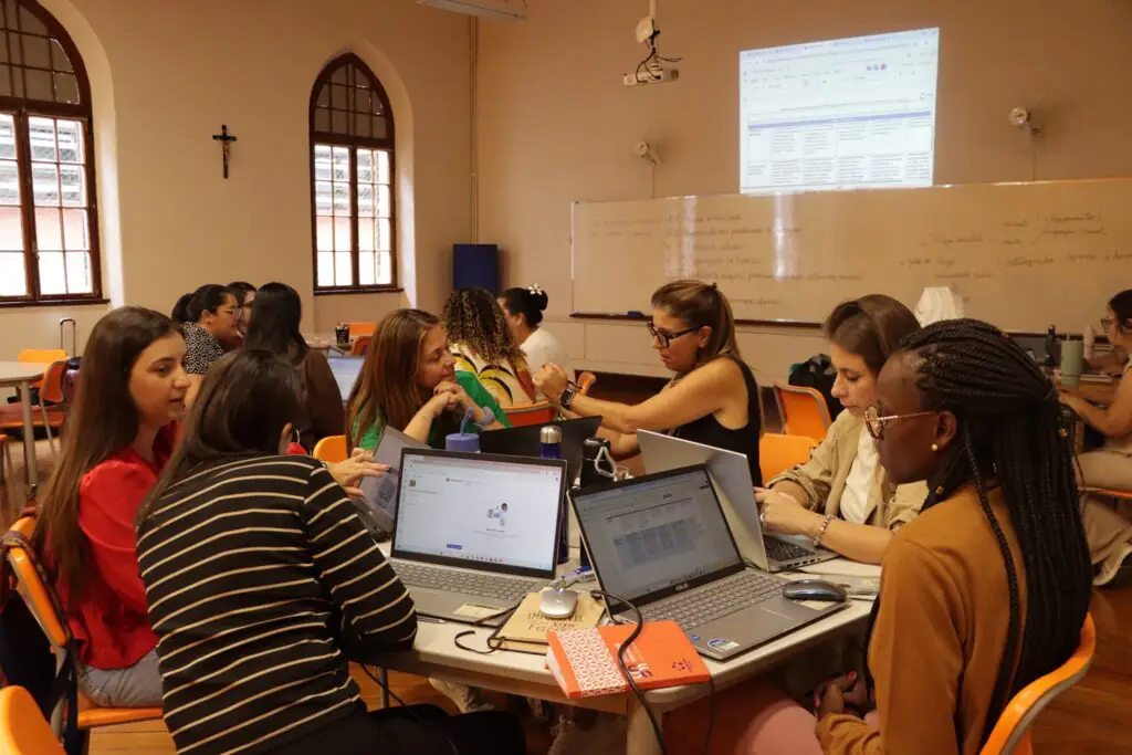 Descrição da imagem: foto de um grupo de educadoras sentadas numa mesa circular com notebooks.