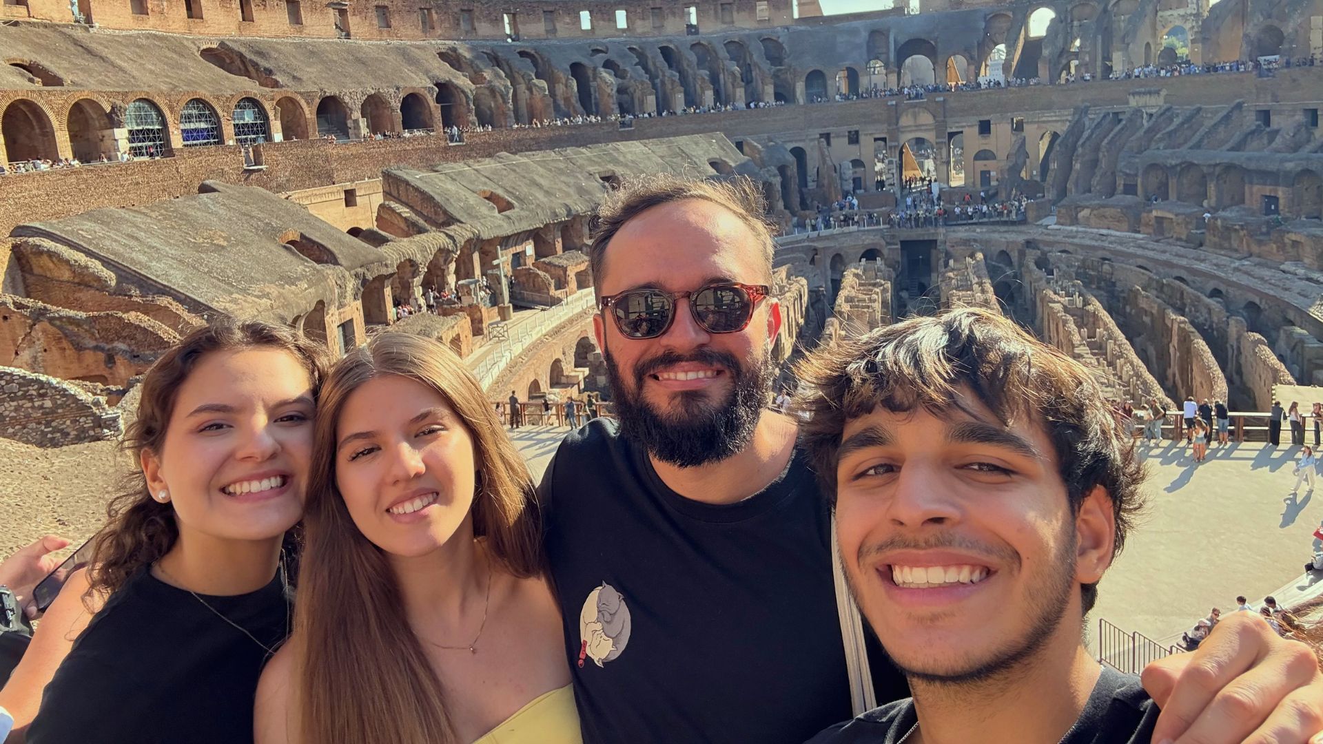 Descrição da imagem: selfie dos três estudantes e o professor Lucas no Coliseu.